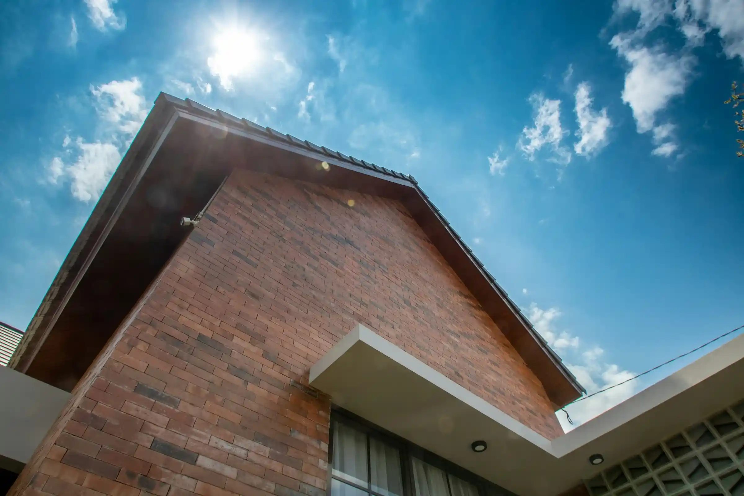 The roofline and brick wall of a house seen from below against a bright sky